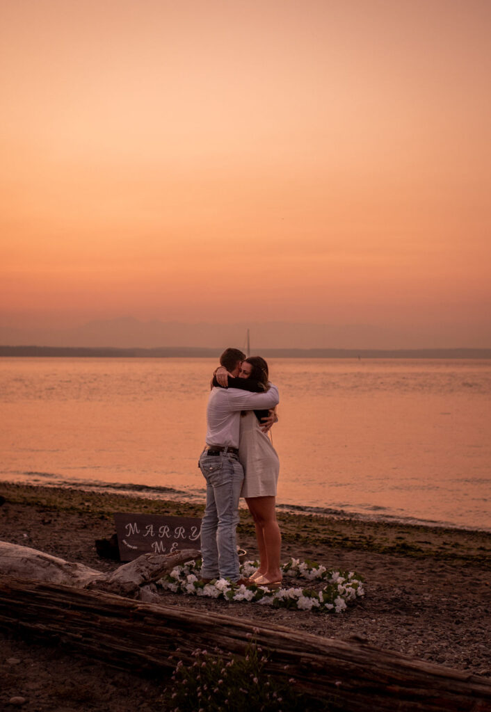 Couple hugging after surprise proposal at Golden Garden Parks in Seattle Washington