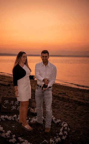 Couple popping champagne during surprise proposal at Golden Garden Parks in Seattle Washington
